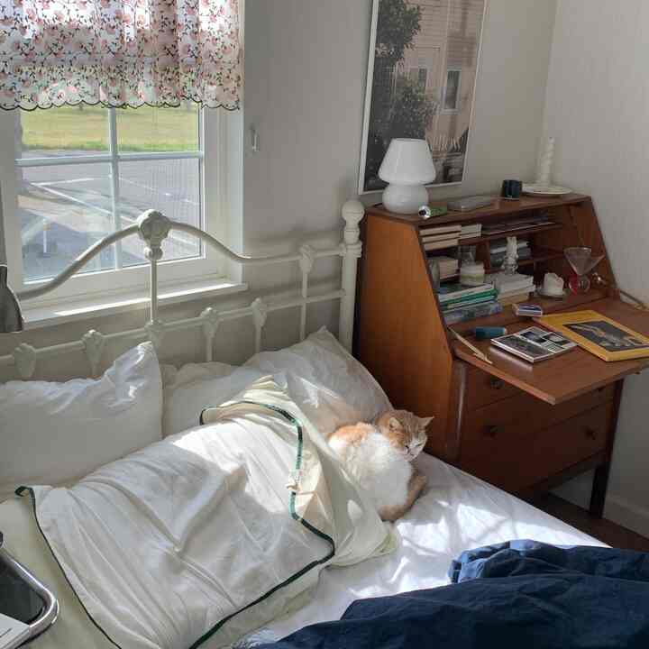 自然光が差し込む白と茶色のトーンの寝室、白い掛け布団カバーとヴィンテージの木製デスクが調和した雰囲気のある空間