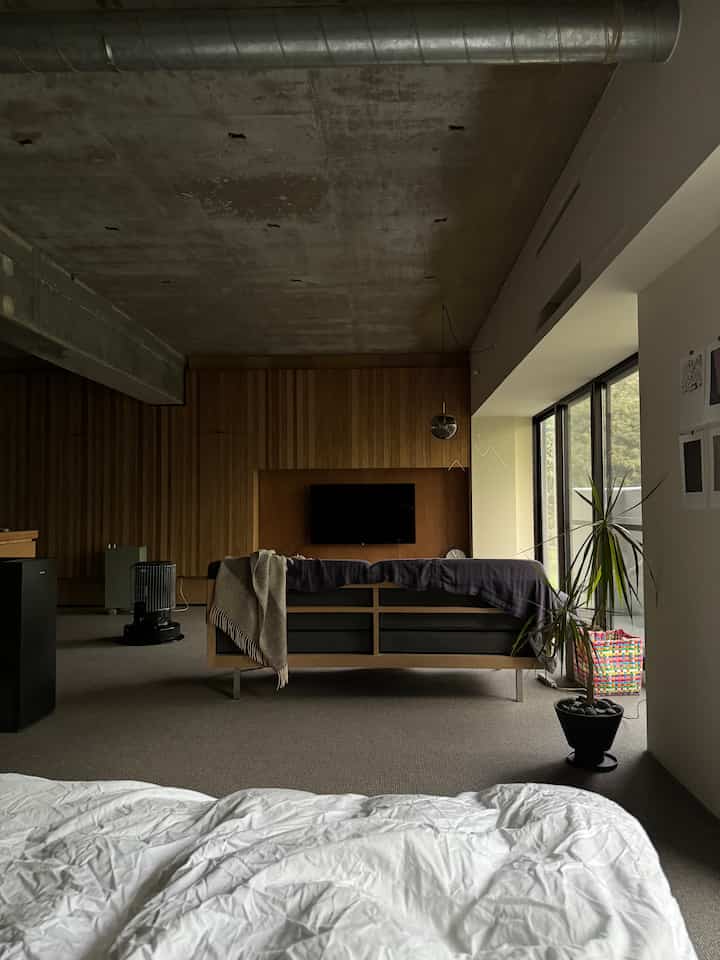 ウッドトーンとナチュラルカラーが特徴の寝室兼リビングスペース、ソファとペンダントライトが配置されたミニマルでモダンな印象のインテリア
