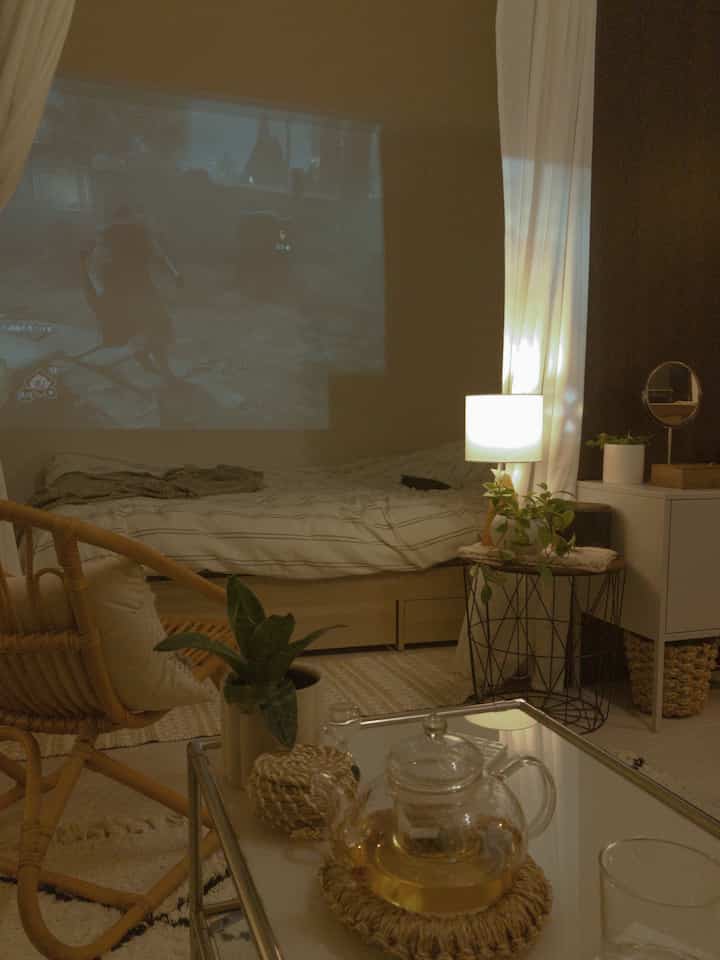 ホワイトとブラウンのトーンで統一された1LDKの寝室、ベッドとラタンチェア、コーヒーテーブル、照明が配置された雰囲気のあるインテリア