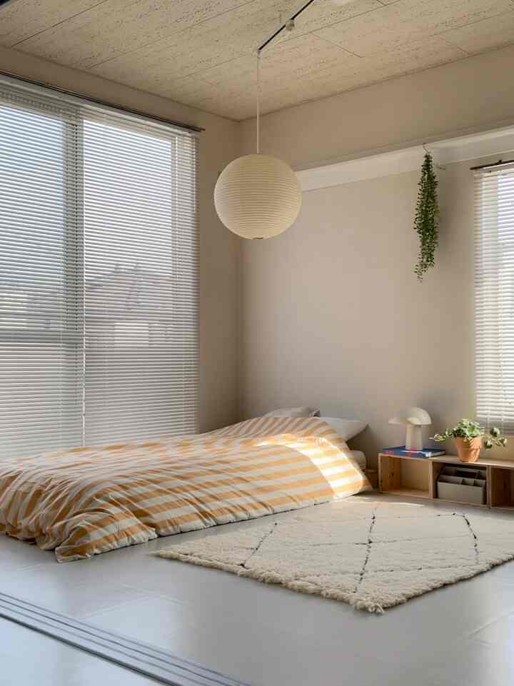 淡いベージュとナチュラルトーンの寝室、低いベッドと植物、ペンダントライトが配置された雰囲気のあるインテリア