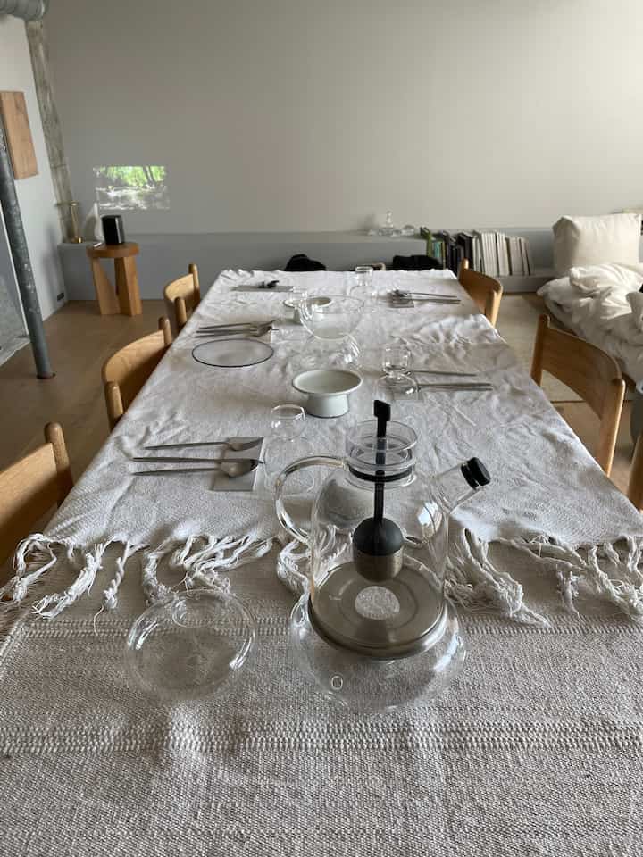 ホワイトのテーブルクロスと透明なガラス食器が配置されたナチュラルトーンのダイニングルーム、ソファとプロジェクターが調和するホームパーティー空間