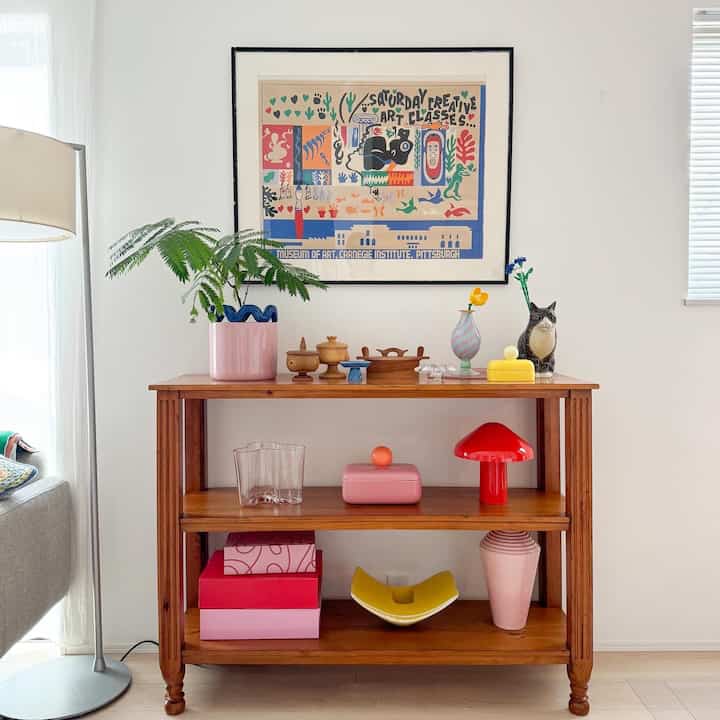 カラフルなヴィンテージ木製棚、花瓶や植物、テーブルランプが配置された明るく居心地の良いリビングルーム