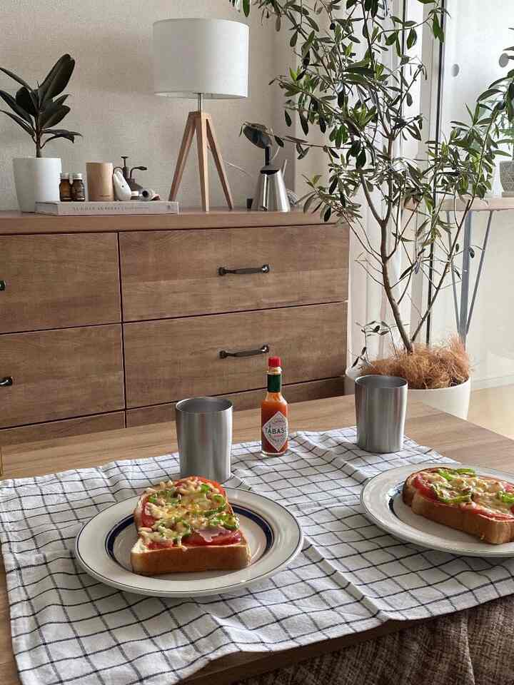 柔らかなナチュラルトーンのキッチン、木製ダイニングテーブルにチェック柄のテーブルランナーとピザトーストが置かれた印象的な食事スペース