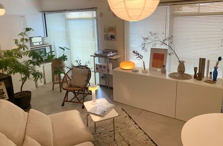 White and natural toned 1LDK living and kitchen space featuring sofa, plants, and warm lighting creating a cozy interior