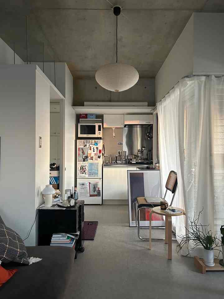 White and gray toned studio apartment living room featuring natural wood dining chairs and sheer curtains, creating a cozy atmosphere
