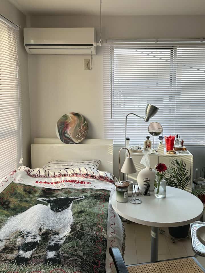 ホワイトとナチュラルカラーの調和が取れた一人暮らしの寝室、大きな窓のブラインドとフロアランプが配置された落ち着いた空間