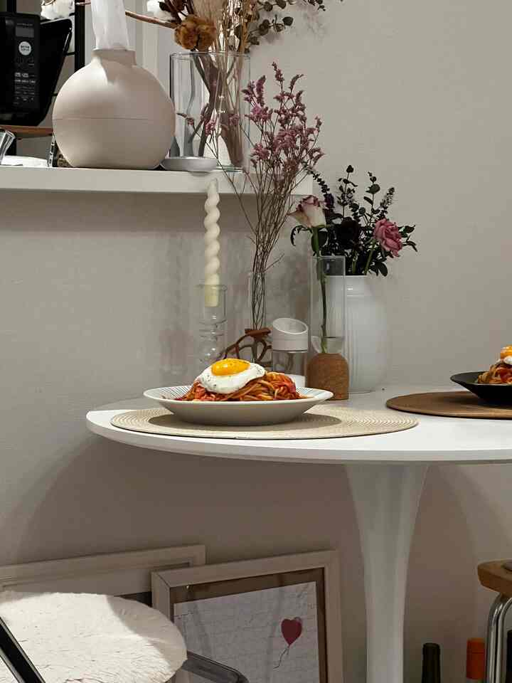 White and natural-toned dining space featuring vases and a round table with plated food, creating a clean home cafe ambiance