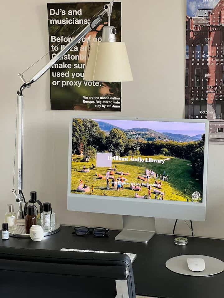 A clean home office featuring a black desk with a silver table lamp and a large white monitor