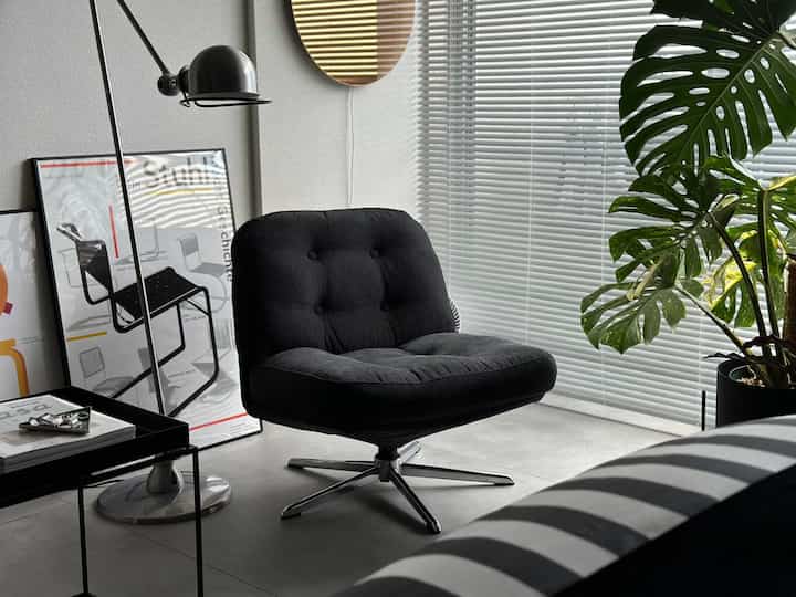 モノトーンでモダンなリビング、黒のアームチェアとフロアランプ、植物が配置された洗練された空間