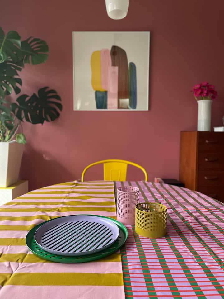 ピンクと黄色を基調としたダイニング、パターン入りのテーブルランナーとトレイが置かれた雰囲気のあるカラフルな空間