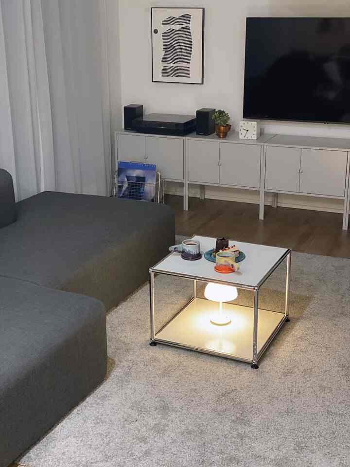 ホワイトとグレーのトーンが特徴のリビング、中央にUSMのローテーブルとテーブルランプが配置されたシンプルモダンな空間