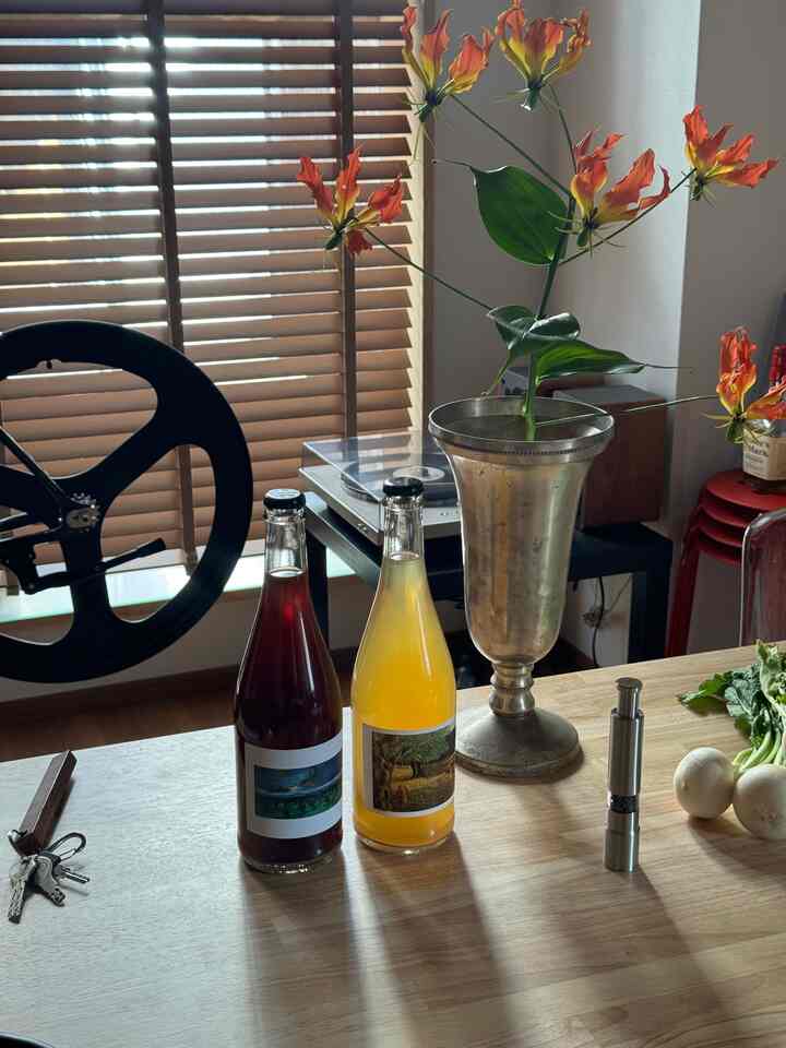 木目調と白色のキッチンスペース、木製ブラインドの前に置かれたテーブルにビール瓶2本とグロリオサの花が飾られた雰囲気のあるインテリア