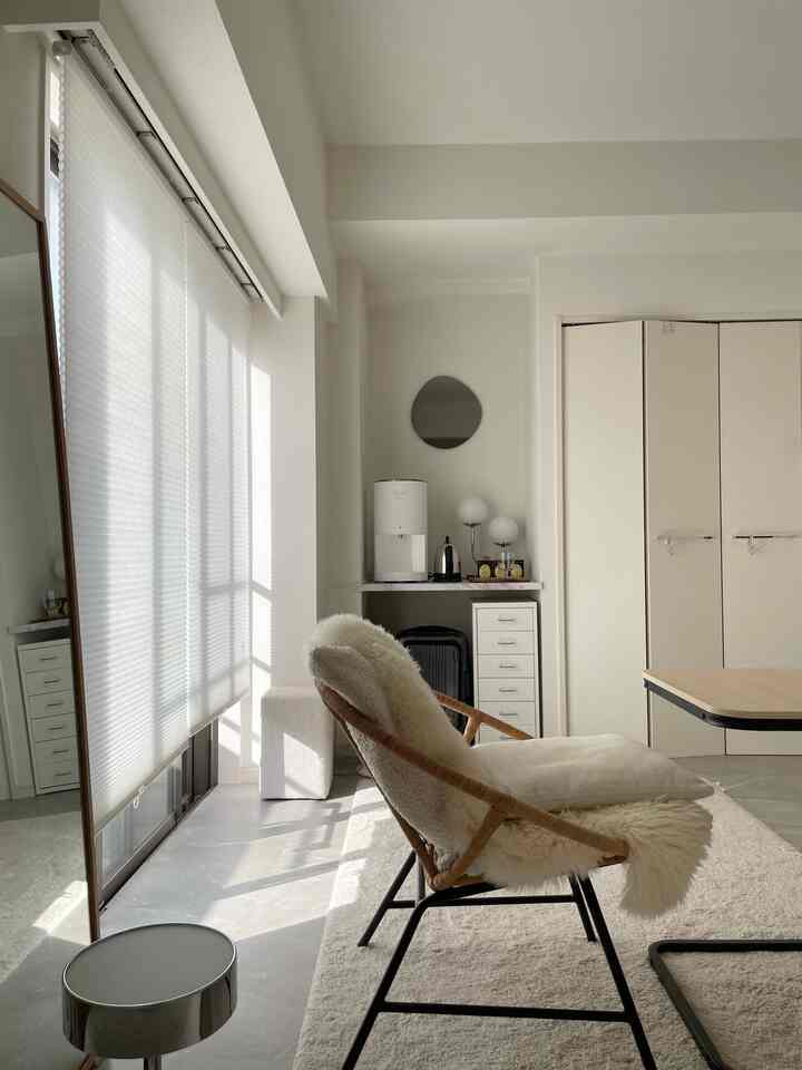 Natural-toned white living room featuring a rattan armchair and built-in closet, showcasing a simple and cozy interior