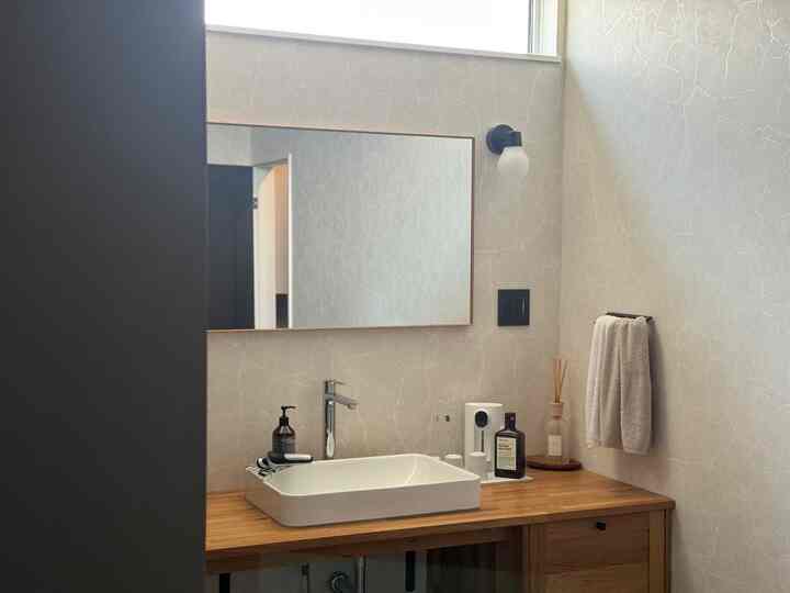 ベージュ色の壁と木目調のカウンターがあるお手洗い、洗面台とディフューザー、マウスウォッシュが配置された清潔感のある空間