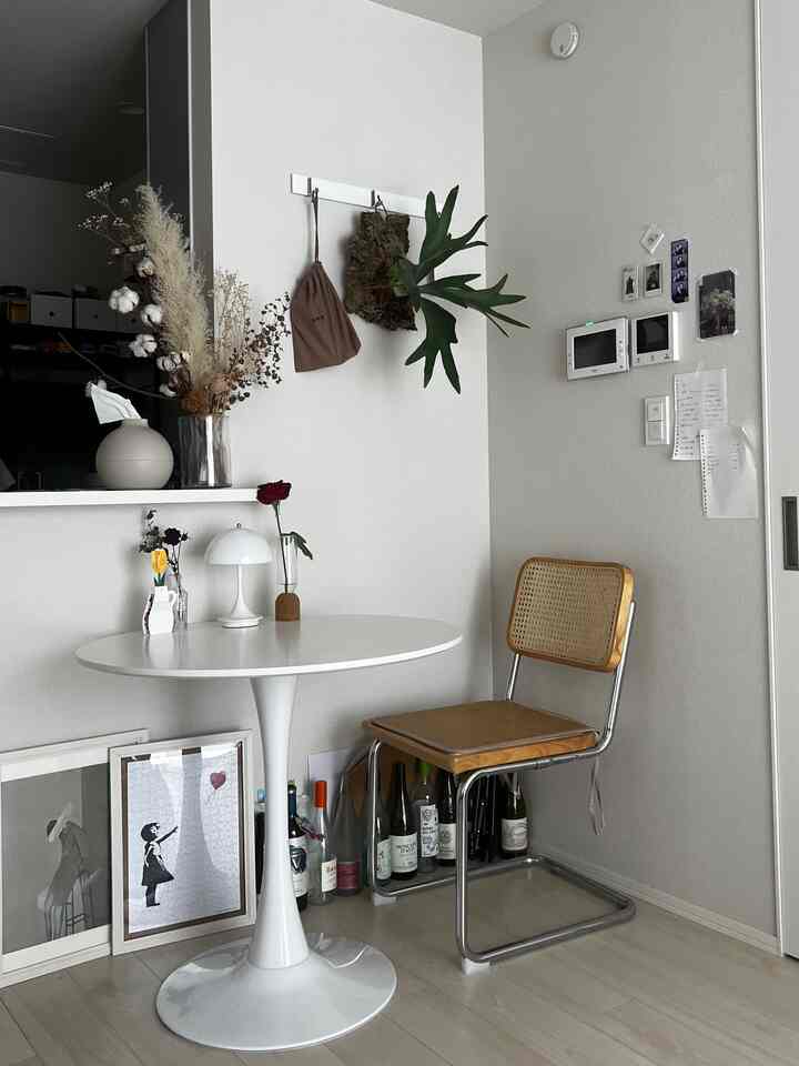 白い壁と丸い白いテーブル、ラタンの椅子が置かれ、緑のコウモリラン観葉植物とドライフラワーが飾られたシンプルでナチュラルな北欧風リビングの印象的なコーナー