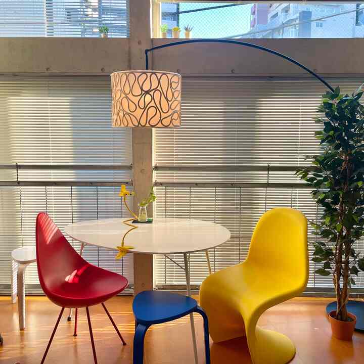 白色のテーブルと鮮やかな椅子、大きなフロアランプと植物が配置されたミッドセンチュリーモダンのダイニングルームの印象的な空間