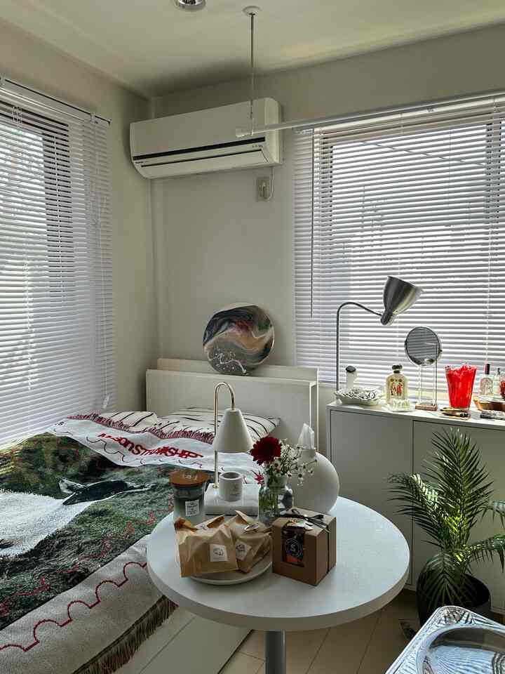 白とナチュラルカラーの一人暮らし寝室、ブラインドと植物が配置された雰囲気のある空間