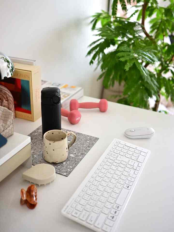 白を基調としたホームオフィス、机上にキーボード、マウス、マグカップ、ピンクのダンベルと植物が配置された雰囲気のある空間