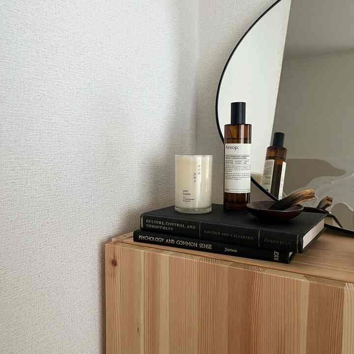 ナチュラルな色調のワンルーム、木製の収納台の上に鏡とオブジェが配置されたシンプルで落ち着いた印象の空間