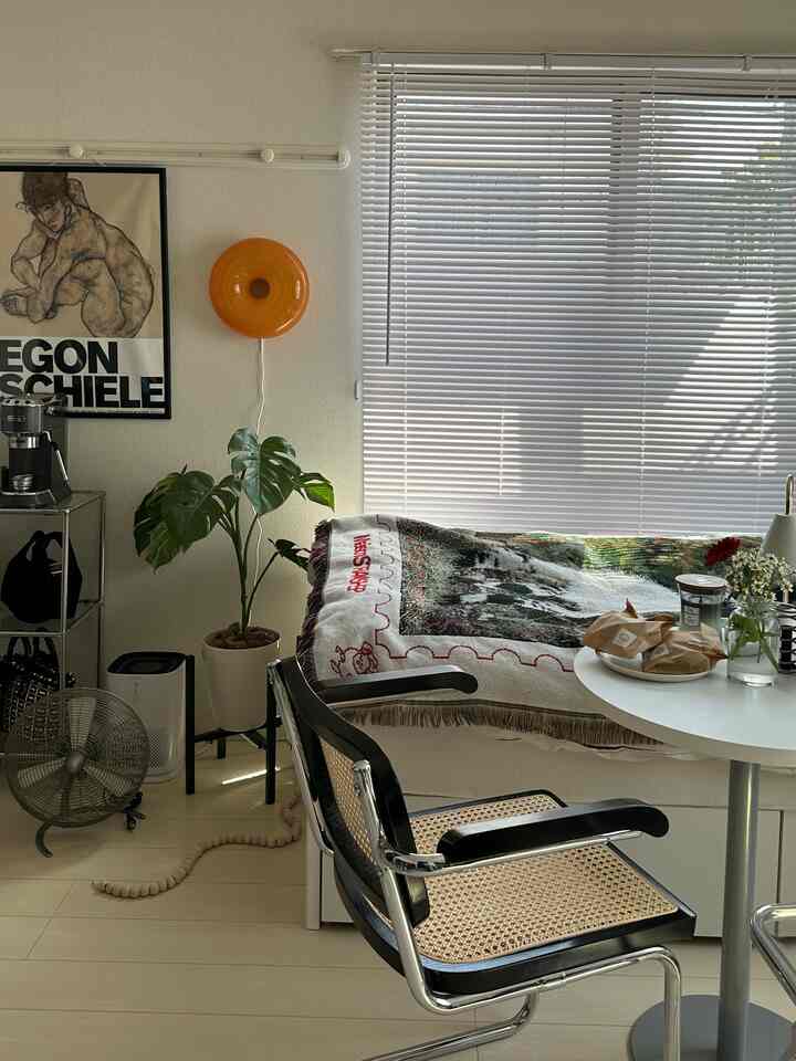 明るい白と茶色のトーンのリビング、ラタンのアームチェアと丸いテーブル、コーヒーメーカーと植物が配置された居心地の良いカフェ風インテリア