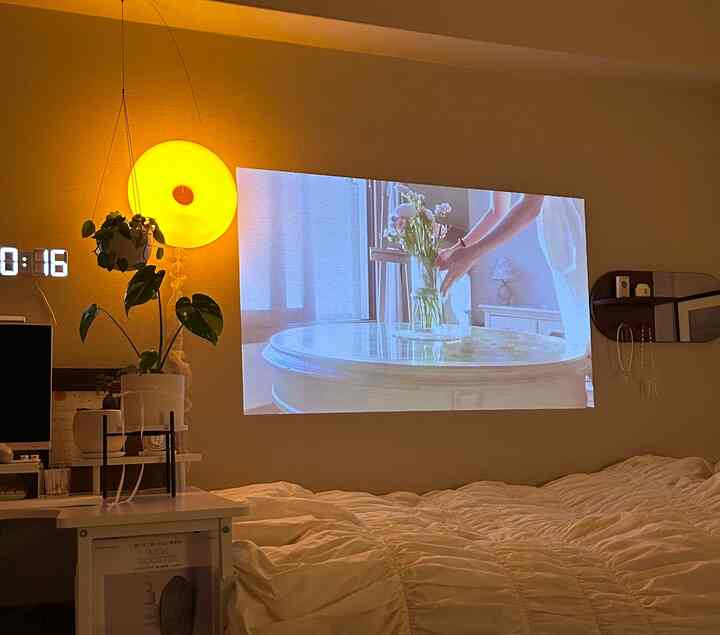 暖かい黄色の壁照明と白い掛け布団カバーがある寝室、壁に映像が映し出された雰囲気のあるインテリア