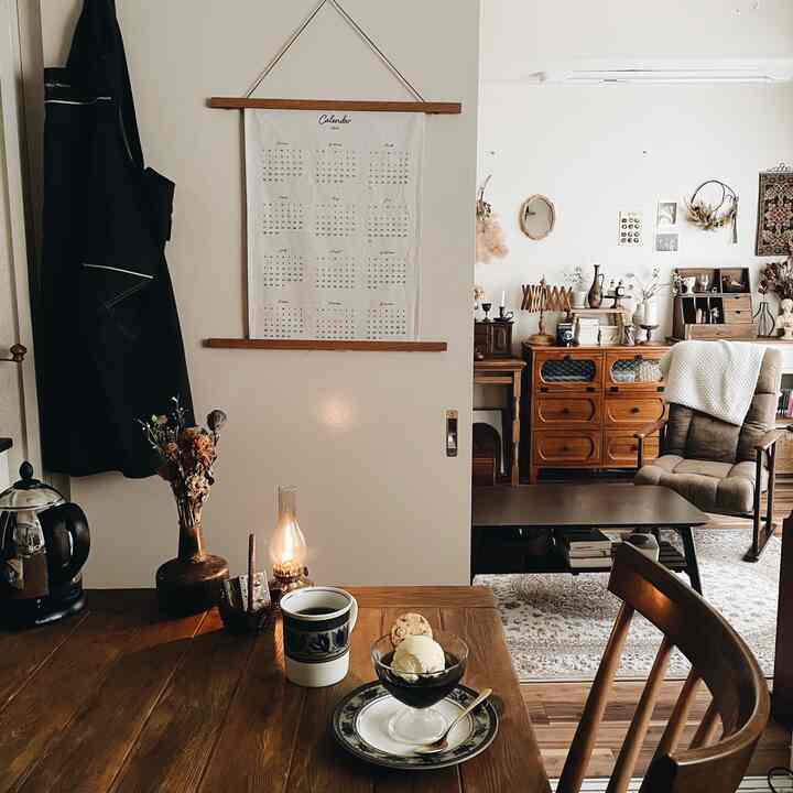 白い壁と茶色の木製ダイニングテーブルが調和した、ヴィンテージ家具とおうちカフェアイテムが配置された雰囲気のあるリビング