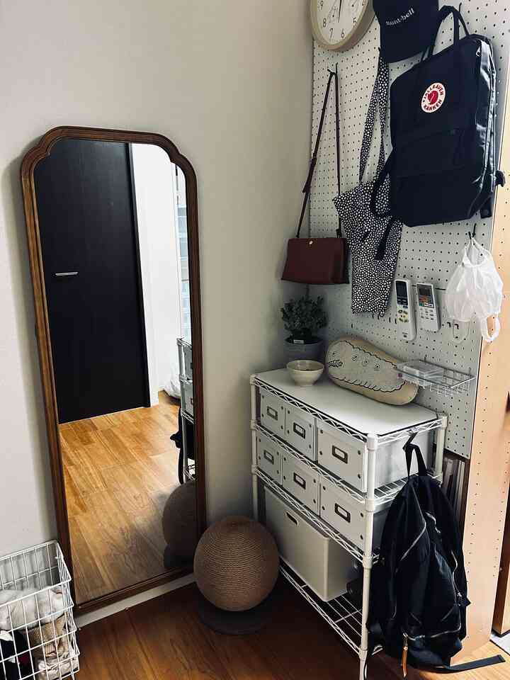 白と茶色のトーンの狭い玄関スペース、壁掛け収納とスチールラックが配置された整理された落ち着きのある空間