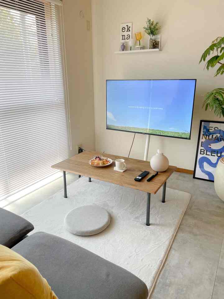 明るいホワイトと木目調が調和したコンパクトなリビング、壁掛けテレビ、低いコーヒーテーブル、グレーのソファが落ち着いた雰囲気を演出