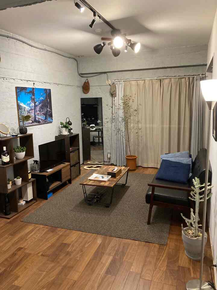Modern natural living room with gray walls and brown wood flooring, featuring black leather sofa and large full-length mirror creating a spacious feel