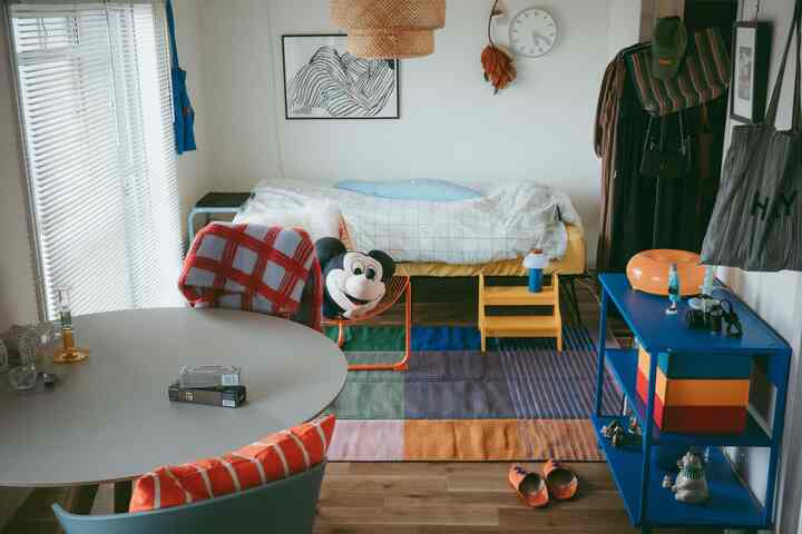 白い背景にカラフルなラグと円形テーブル、ベッドが配置された温かみのあるワンルーム空間