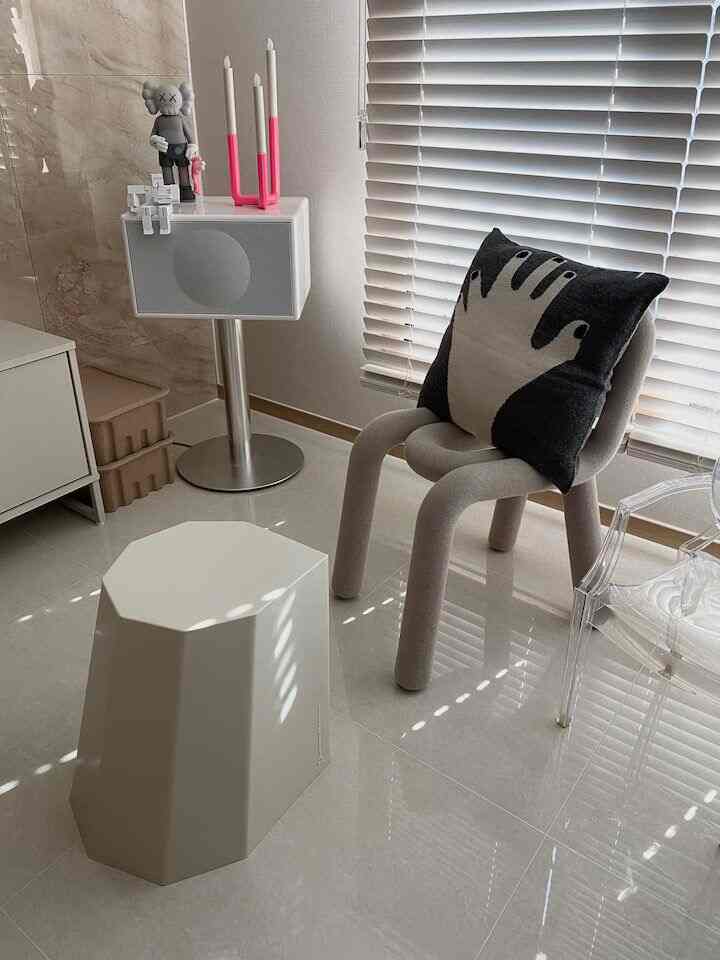 Beige and white toned living space featuring a modern stool, transparent chair, and cushion in a clean interior