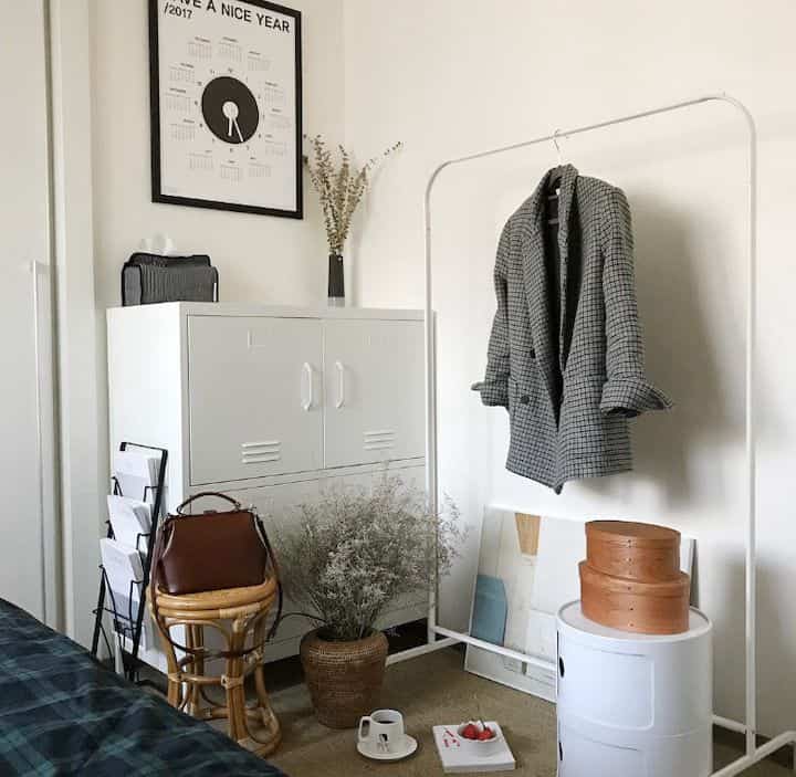 White and beige toned bedroom featuring storage cabinet, coat rack, and natural decor elements in a simple setting