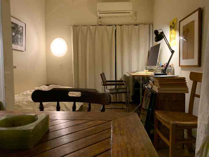 アイボリーのカーテンとブラウンの木製ダイニングテーブル、デスクが配置されたシンプルなワンルームのホームオフィス空間