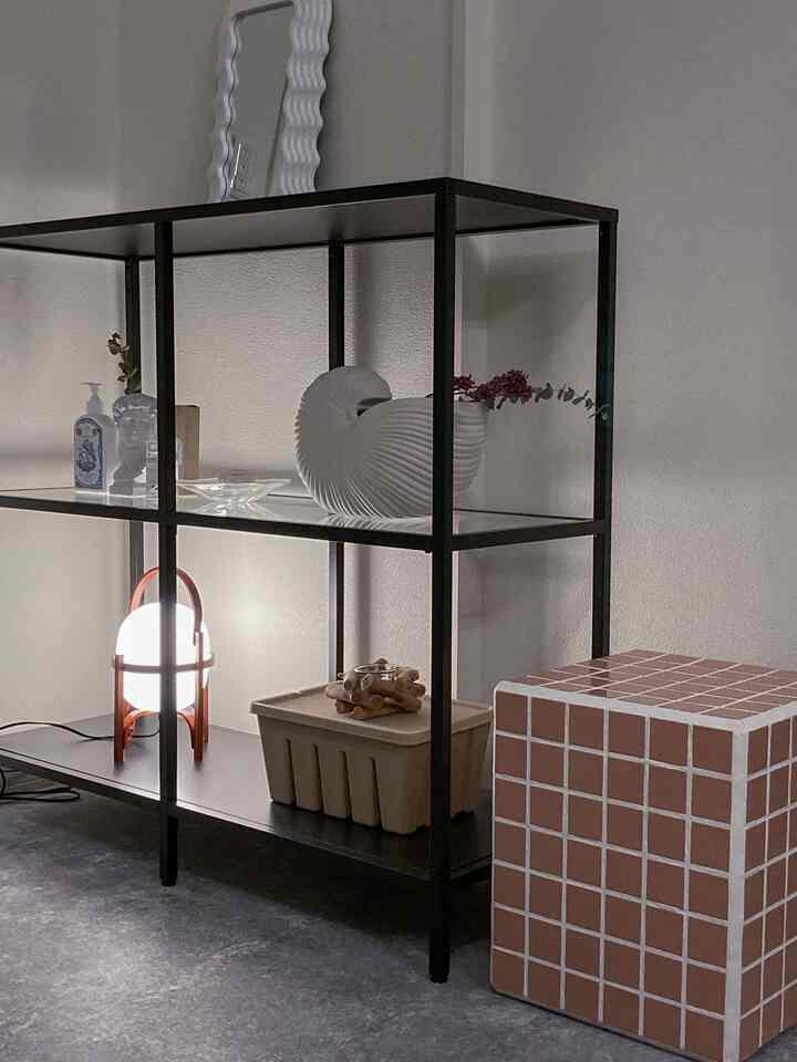 モノトーンのリビング、黒いメタル棚と独特な照明、ピンクのタイルキューブが配置されたシンプルなインテリア