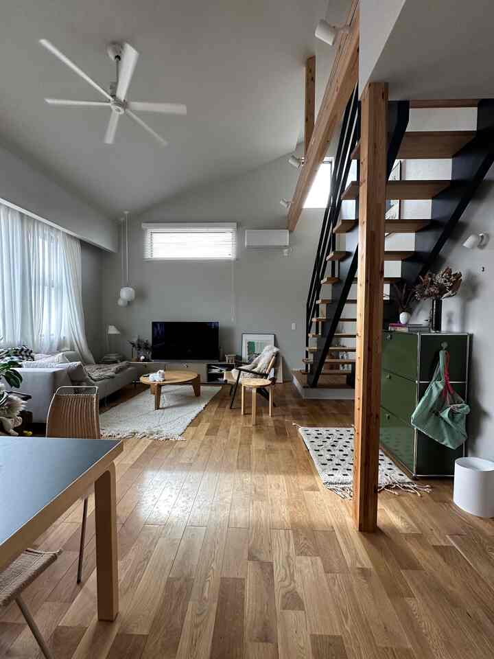 明るいホワイトと木目調が調和したリビング、モダンでナチュラルな家具と階段が配置された広くてすっきりとした空間