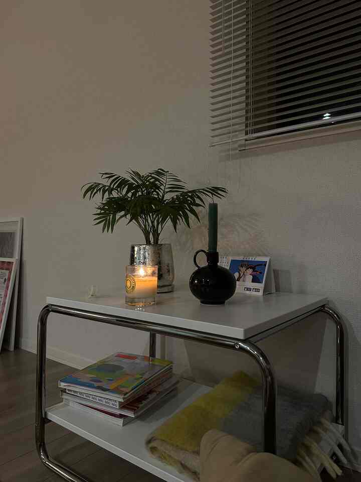 Cozy bedroom corner with white and black-toned side table featuring a plant and lit candle