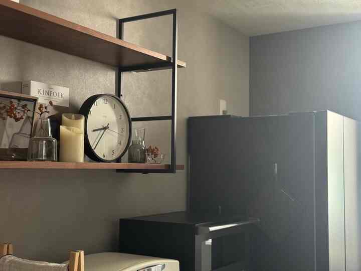 Natural modern kitchen interior with wood tone shelving and black refrigerator, featuring a design clock and LED candle lights centrally positioned