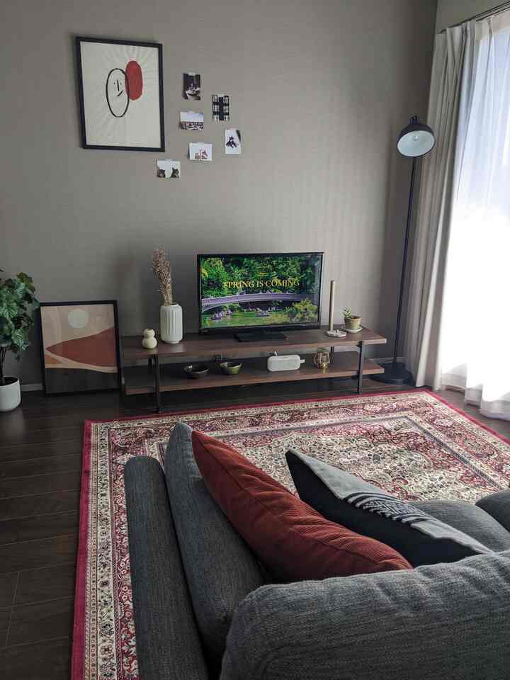 ベージュ色調のリビング、ダークグレーのソファと木製テレビ台が配置された落ち着いた雰囲気の空間