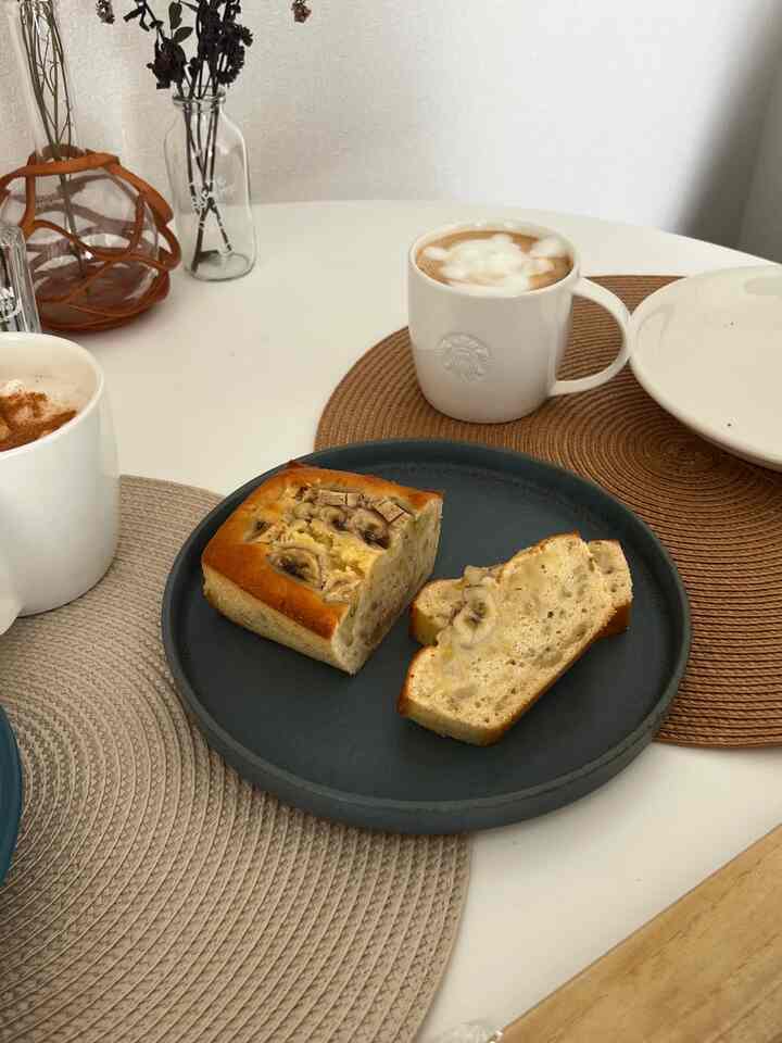 ナチュラルな色調の小さなリビング、丸いローテーブルにおうちカフェの飲み物とバナナパウンドケーキが置かれたシンプルな雰囲気のインテリア