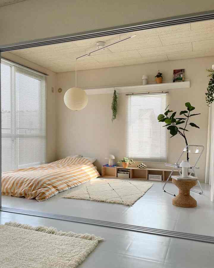 白とベージュのトーンのコンパクトな部屋、低いベッドとコルクスツールが配置され、自然な雰囲気のあるインテリア