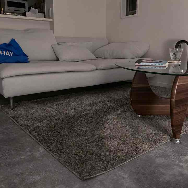 グレーのラグの上にガラスと木製脚のコーヒーテーブルと白いセクショナルソファが配置されたモノトーンの一人暮らしリビング、夜のムードで構成されたインテリア