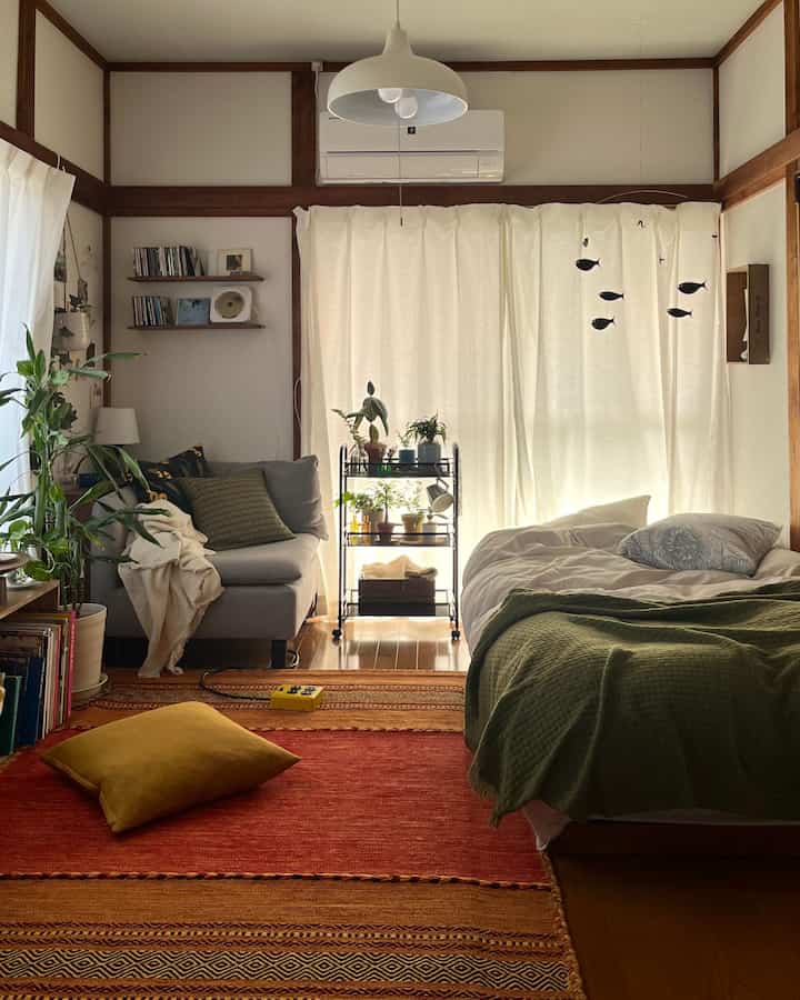 Natural-toned single household living and bedroom space featuring gray sofa and green bedding with cozy atmosphere