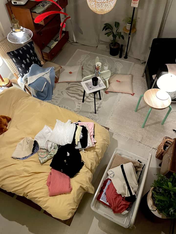 ナチュラルな色調の狭いリビング、黄色いベッドとガラスのテーブル、木製スツールが配置された雰囲気のある空間