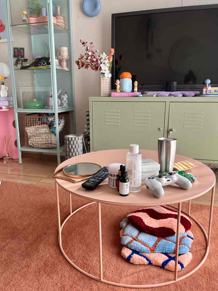 A cozy living room with pink tones and natural wood hues featuring a round coffee table, green cabinet, and display cabinet