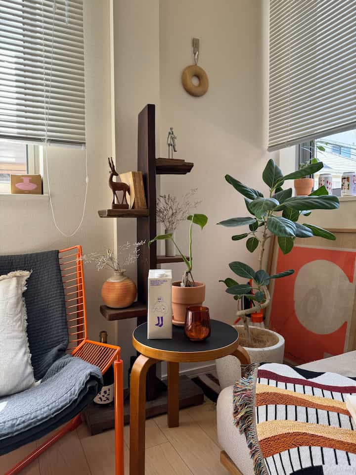 明るいナチュラルカラーの1LDKリビング、オレンジのスツールと植物が配置された雰囲気のある空間