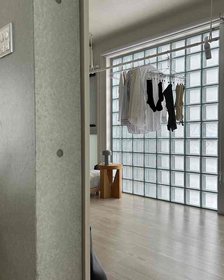 Small studio veranda with white and wood tones, featuring a stool with a table lamp and clothes hanging on a drying rack, creating a natural atmosphere