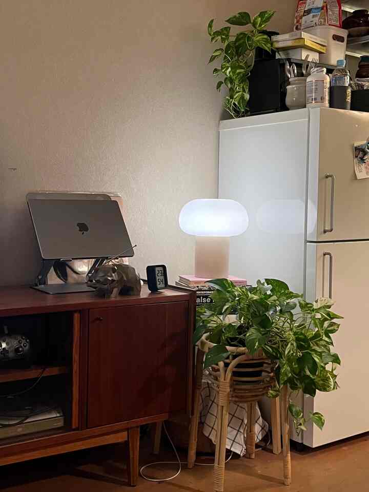 白とベージュのトーンのホームオフィス、ノートパソコンスタンドとテーブルランプ、植物が配置された雰囲気のある作業スペース