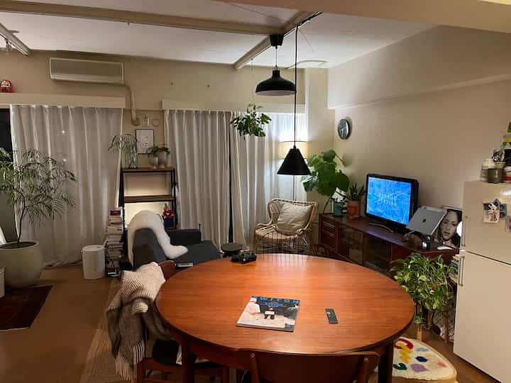 Natural wood tones and white 2-person living room featuring multiple plants and rattan chair, creating cozy atmosphere