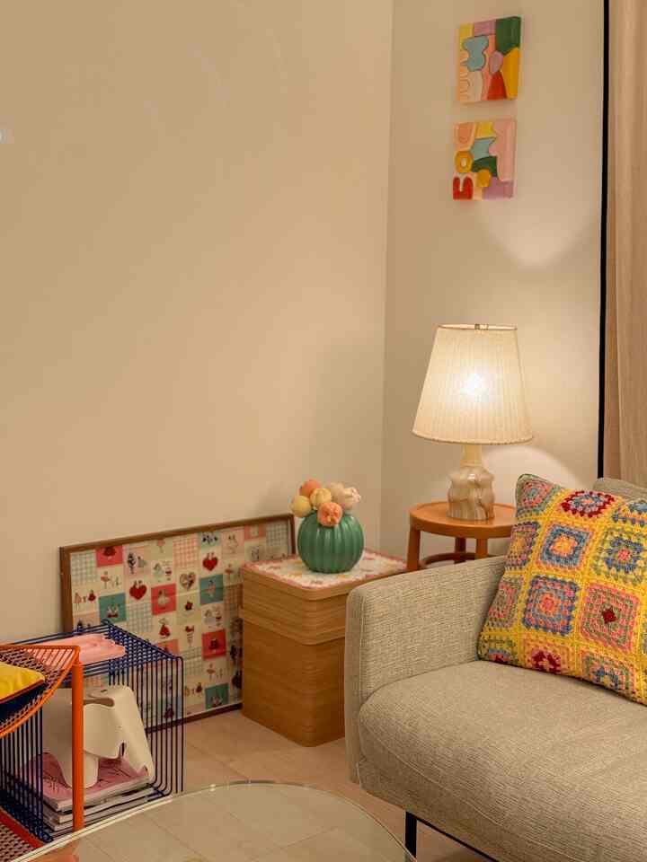 ベージュと木目調が調和したリビング、カラフルなアートと編み物クッションが印象的な居心地の良い空間