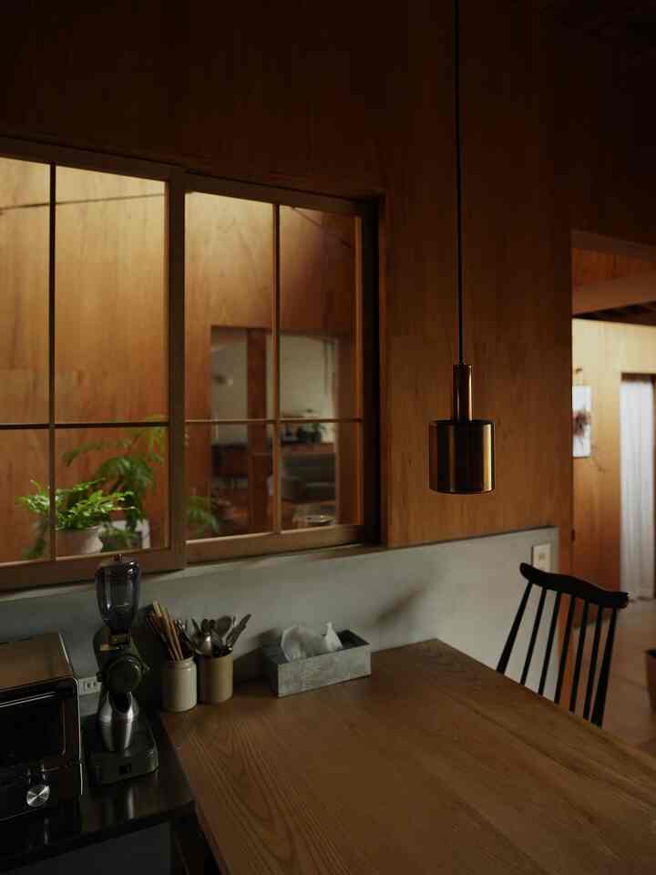 暖かい木目調の壁とダイニングテーブルがあるキッチンスペース、コーヒーグラインダーとペンダントライトが見える雰囲気のあるおうちカフェ